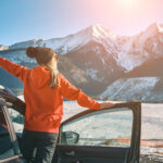 Osoba vystupující z auta s výhledem na zasněžené hory